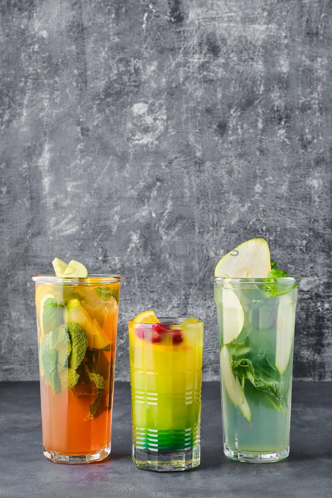 Three glasses with fruit refreshing drink on gray shabby background