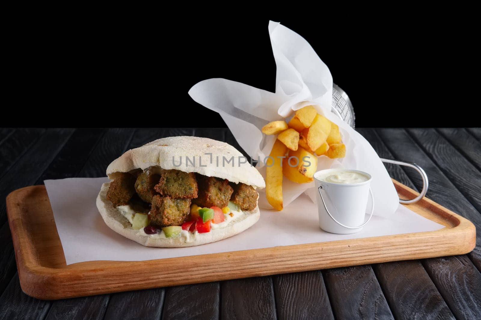 Pita bread with falafel, vegetables and fried potatos on wooden plate