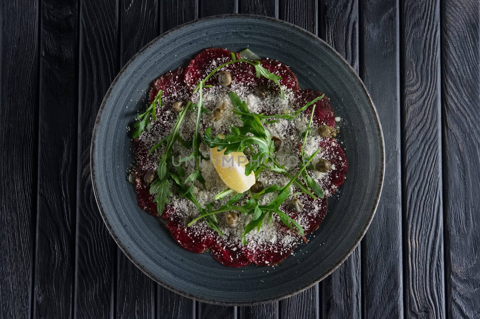 Top view of beef carpaccio with grated cheese, capers, lemon and ruccola