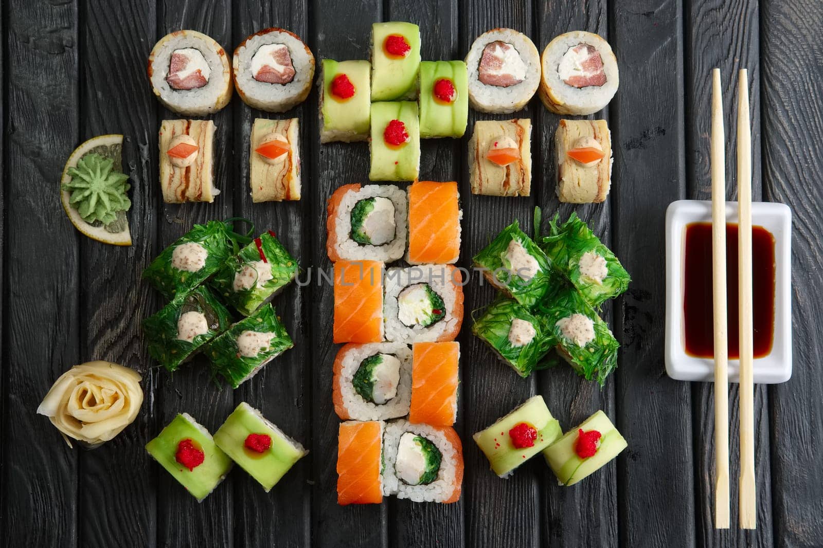 Big set of rolls, soy sauce and chopsticks (hashi) on dark background, top view
