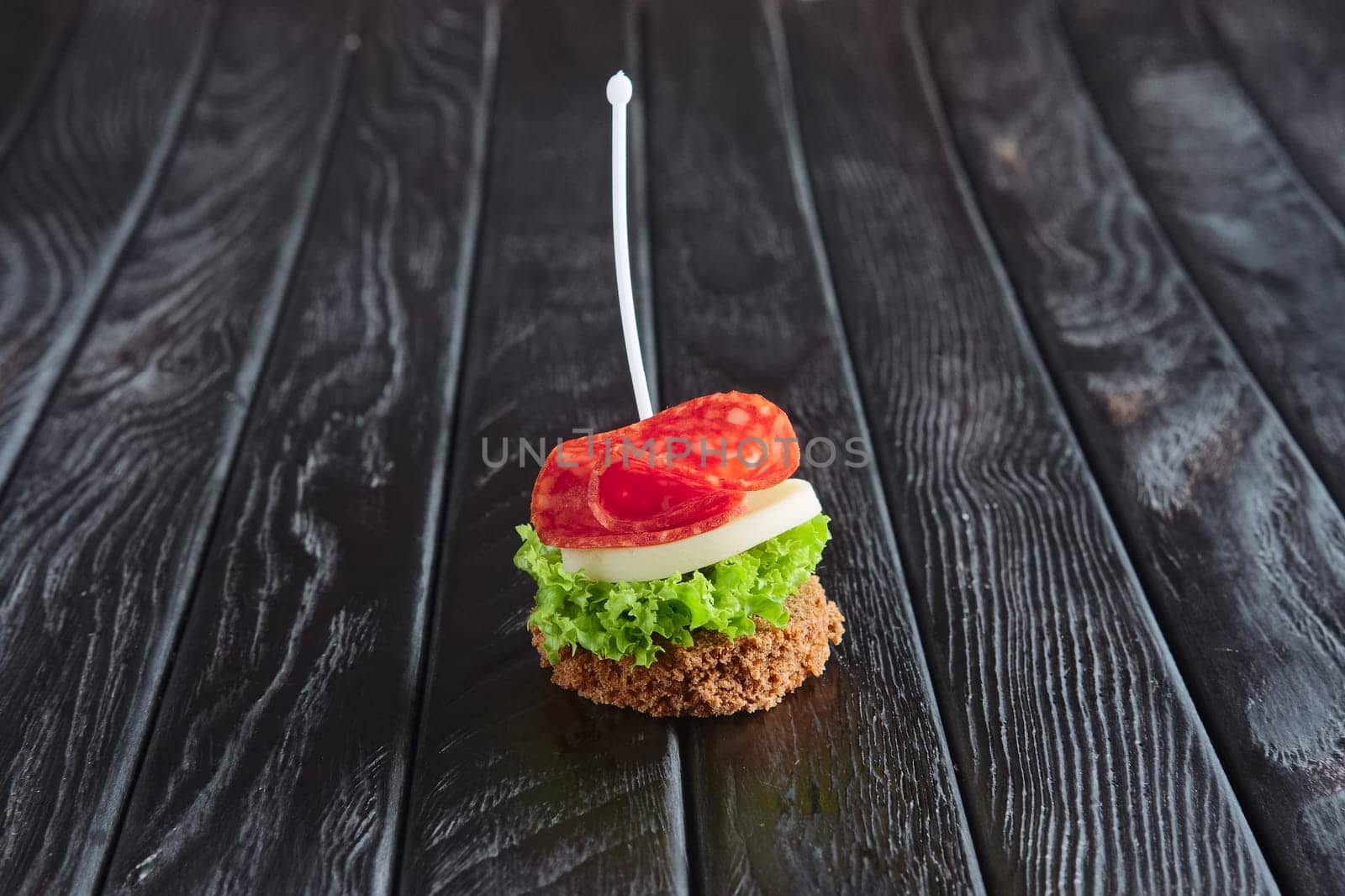 Appetizer for reception. Small sandwich with sausage, sheese and salad leaf on skewer