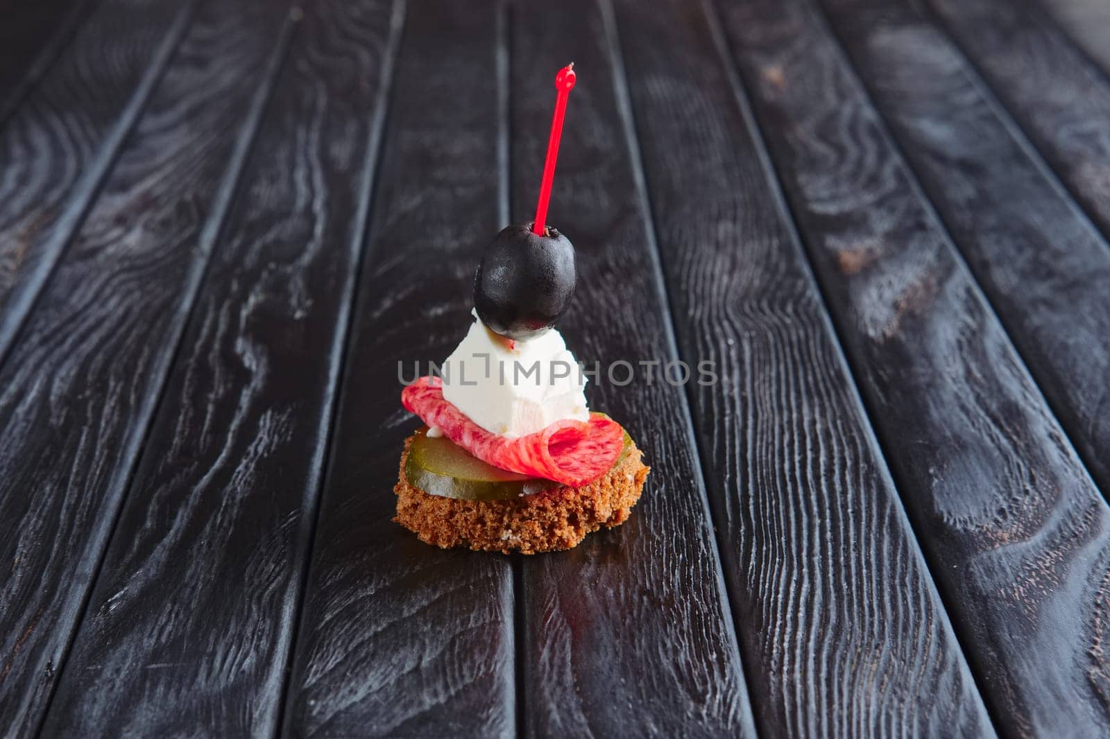 Appetizer for reception. Small sandwich with sausage, sheese and pickled cucumber and olive on skewer