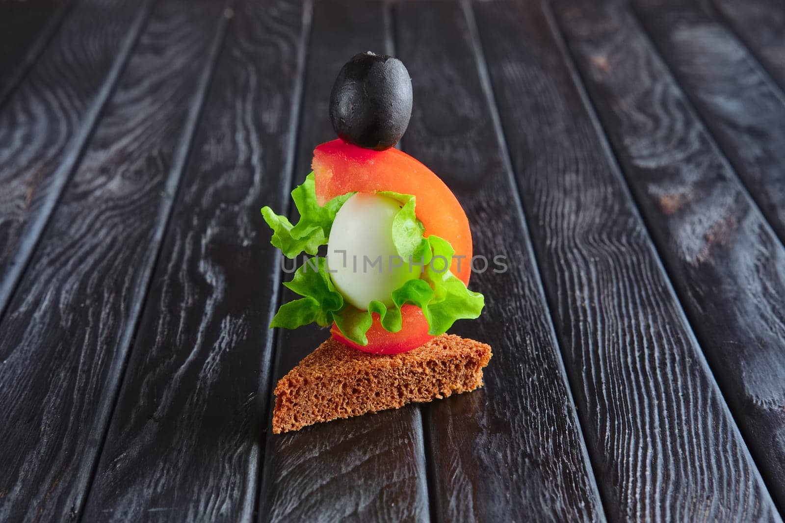 Appetizer for reception. Brown bread with quail egg, tomato, salad leaf and olive on skewer