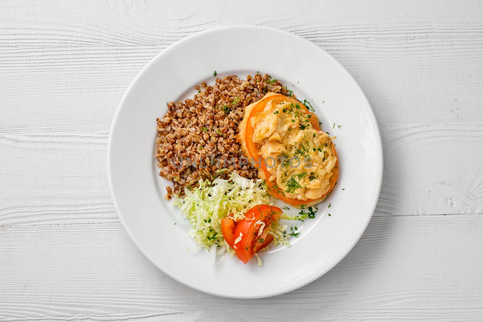 Top view of plate of chopped meat backed with tomato with buckwheat and cabbage salad