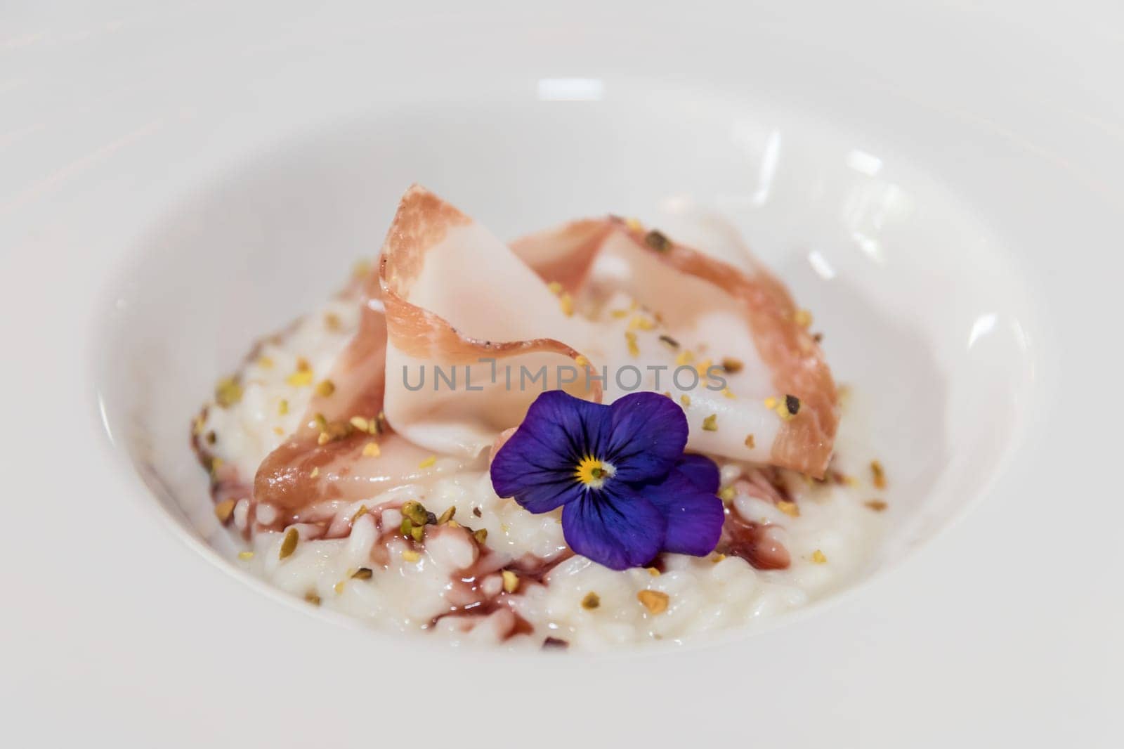 Risotto with pistachio and bacon on white plate, decorated with purple flower.