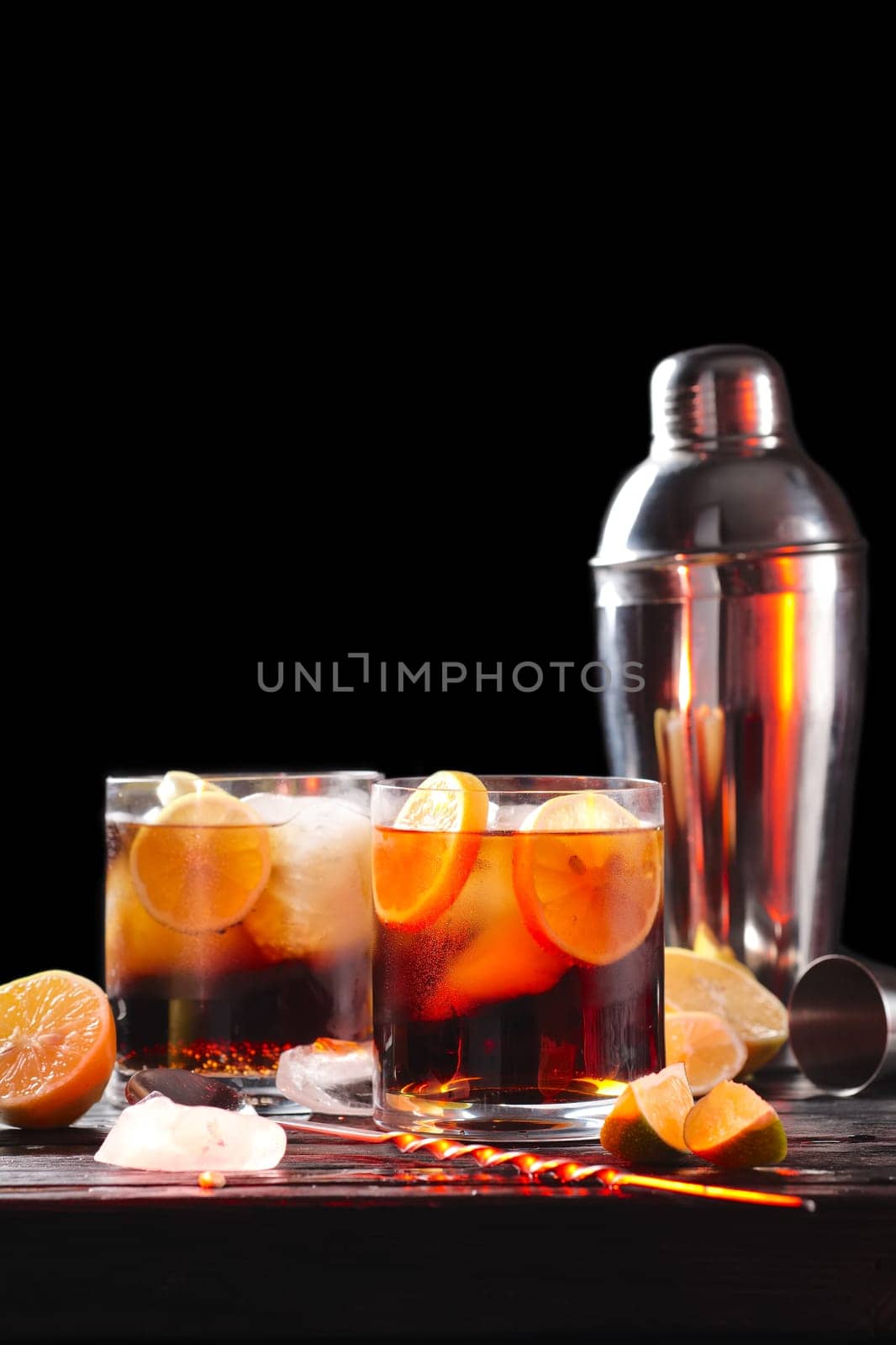 Selective focus composition with rum and cola cocktail served with  citrus on rough paper and fabrick over the wooden table with pieces of ice