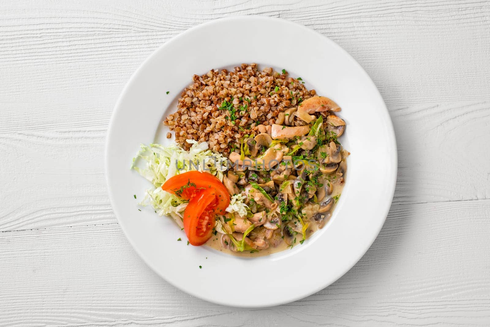 Top view of plate with chicken goulash, mushroom, buckwheat and tomato cabbage salad
