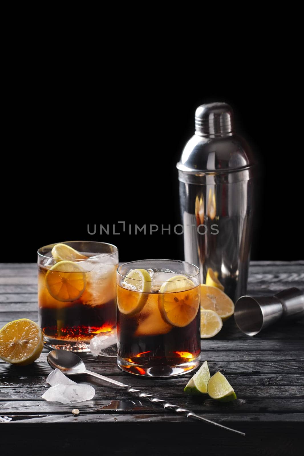 Selective focus composition with rum and cola cocktail served with  citrus on rough paper and fabrick over the wooden table with pieces of ice