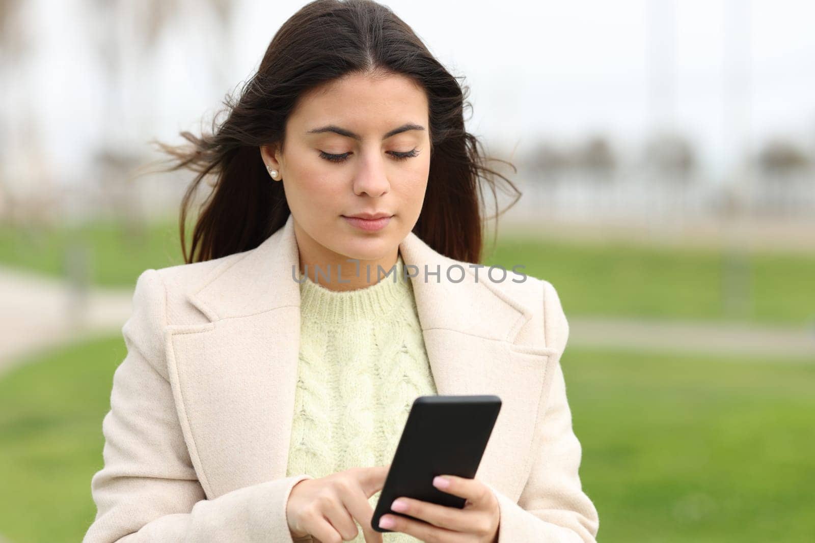 Serious woman walking using smart phone in a park in winter