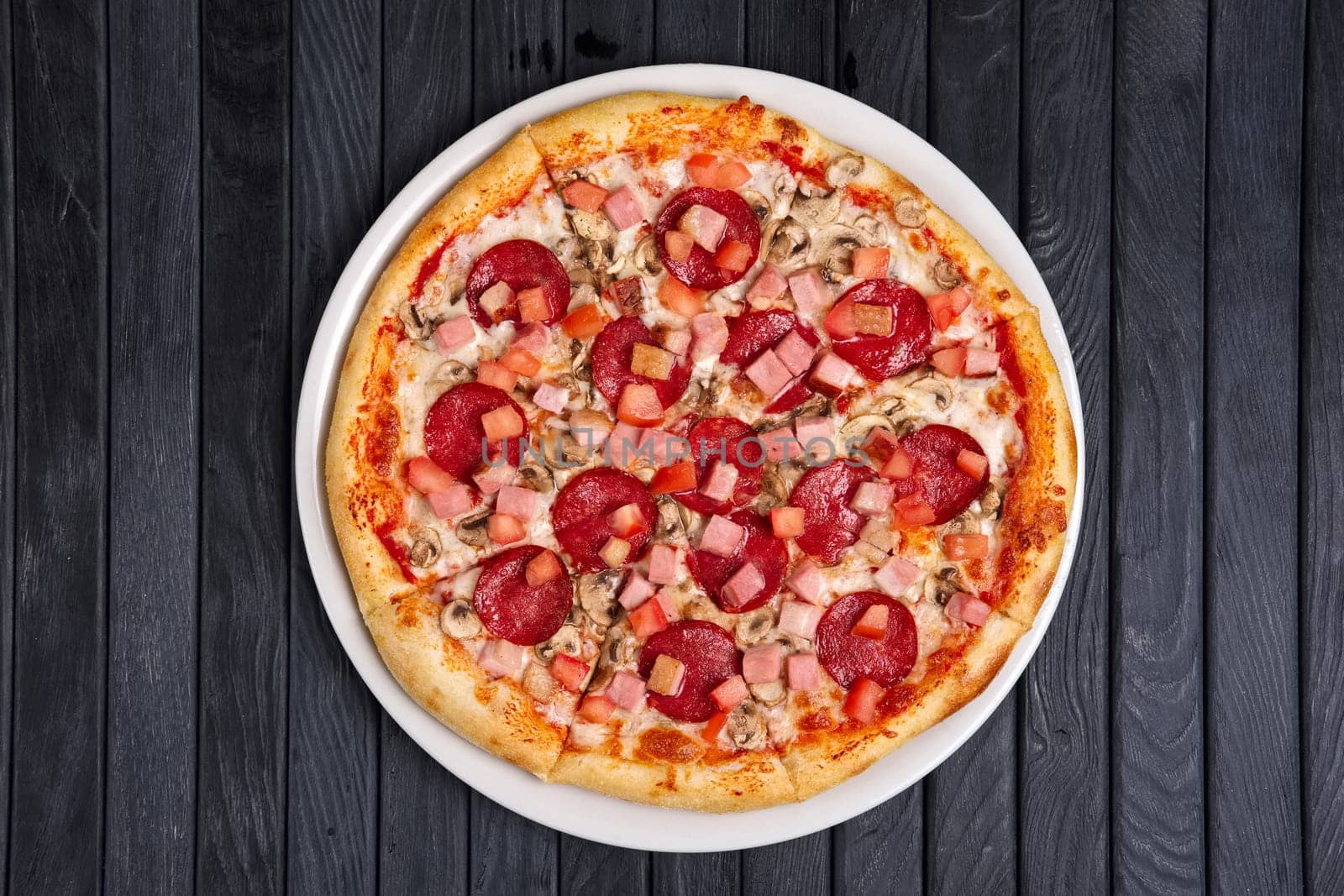 Top view of pizza with sausage, ham and tomato