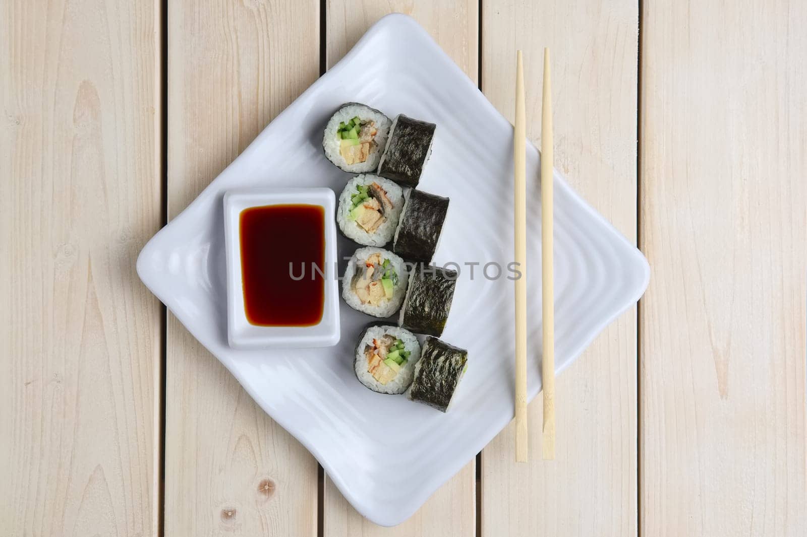 Top view of rolls with salmon, avocado and cucumber on plate with soy sauce and hashi