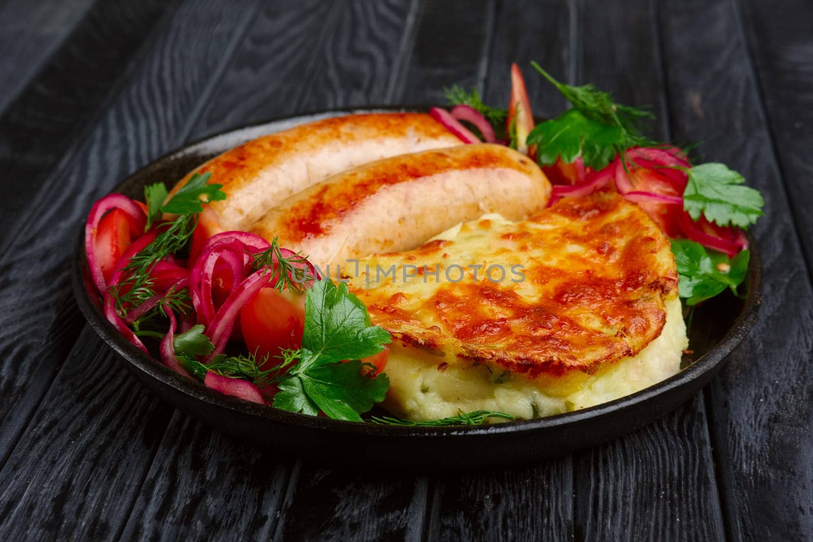 Fried homemade sausage with fried mashed potato, pickled onion and tomato