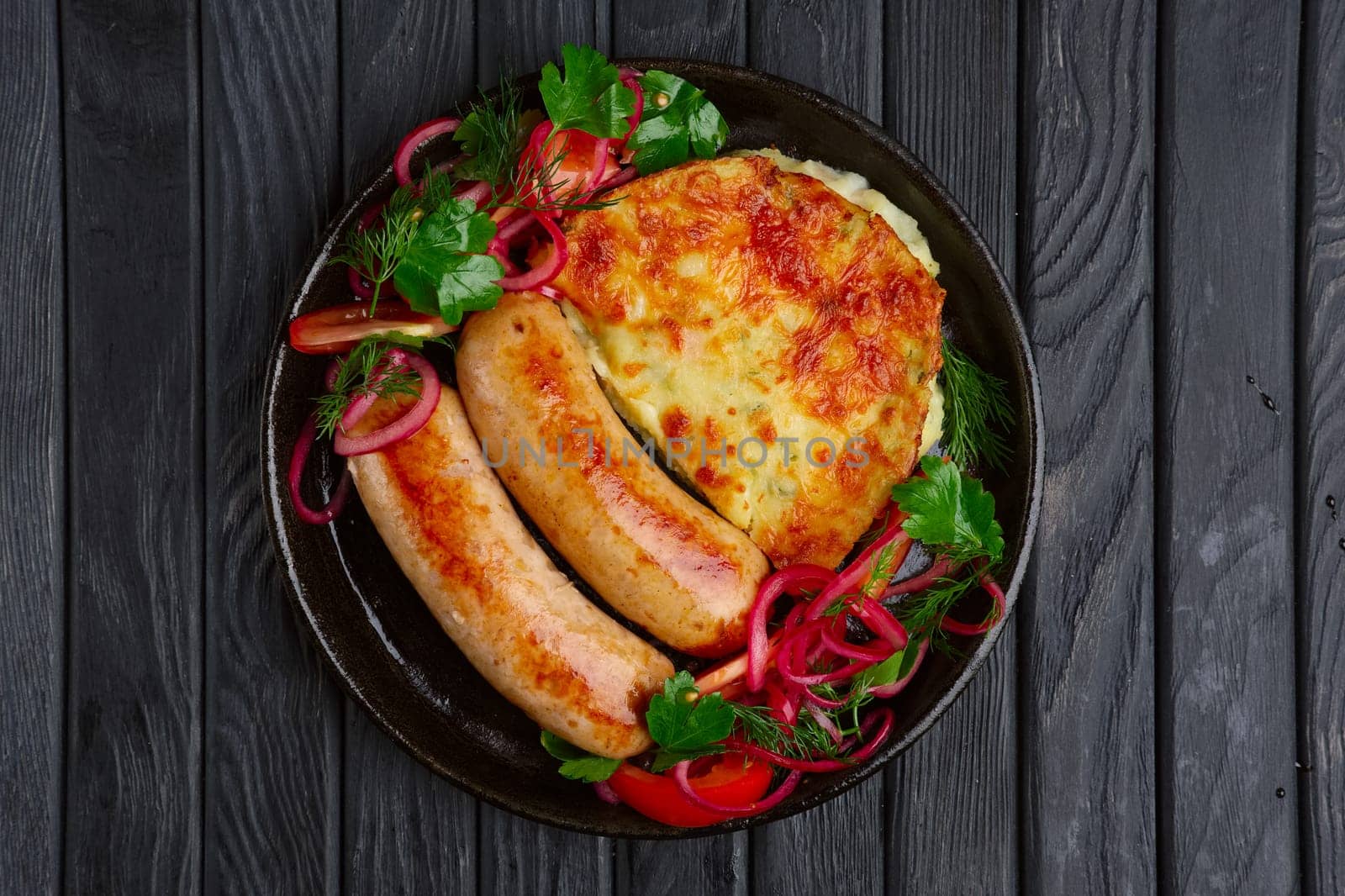 Fried homemade sausage with fried mashed potato, pickled onion and tomato