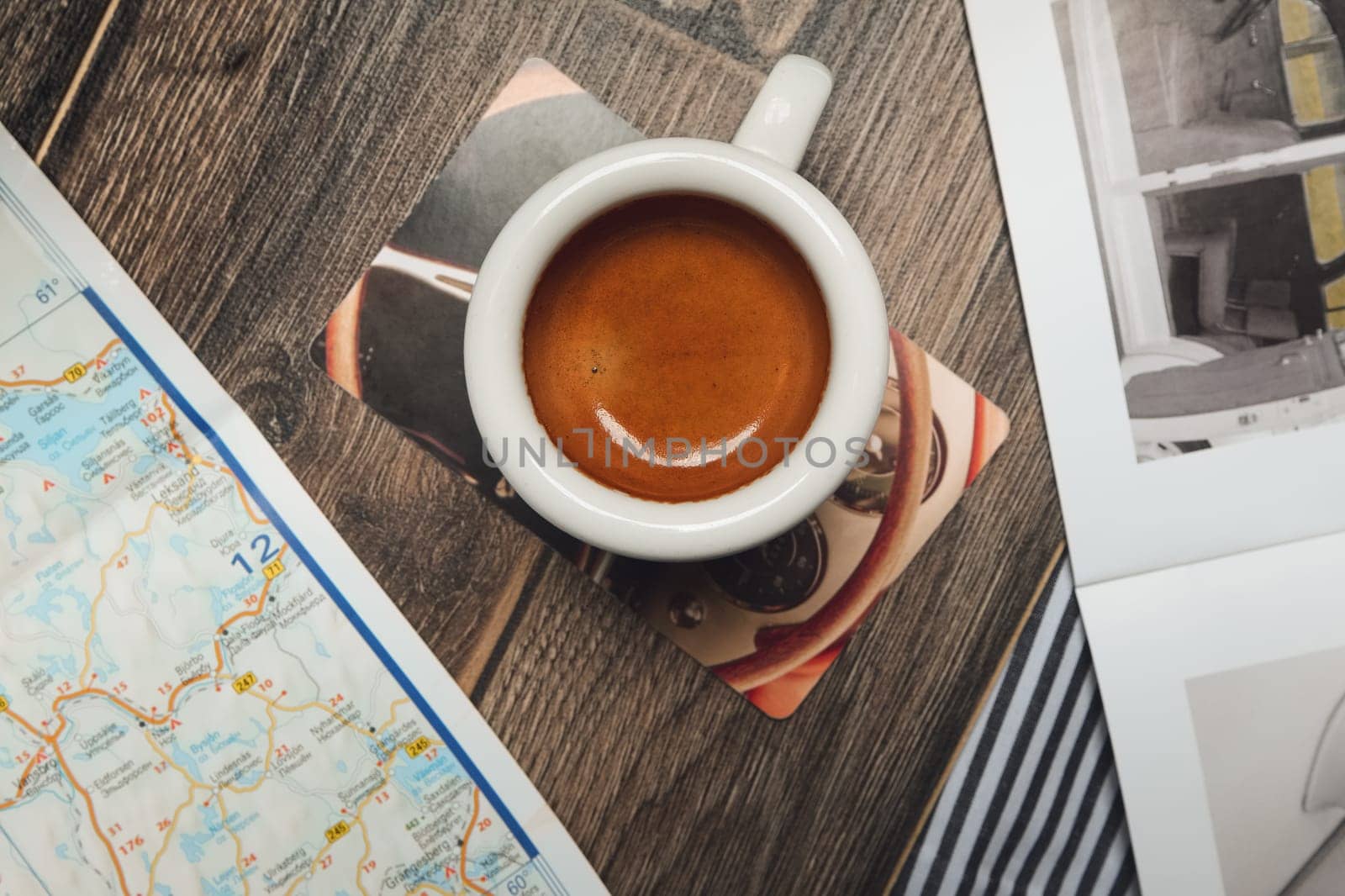 Cup of espresso near map and magazine on the table. Top point of view.