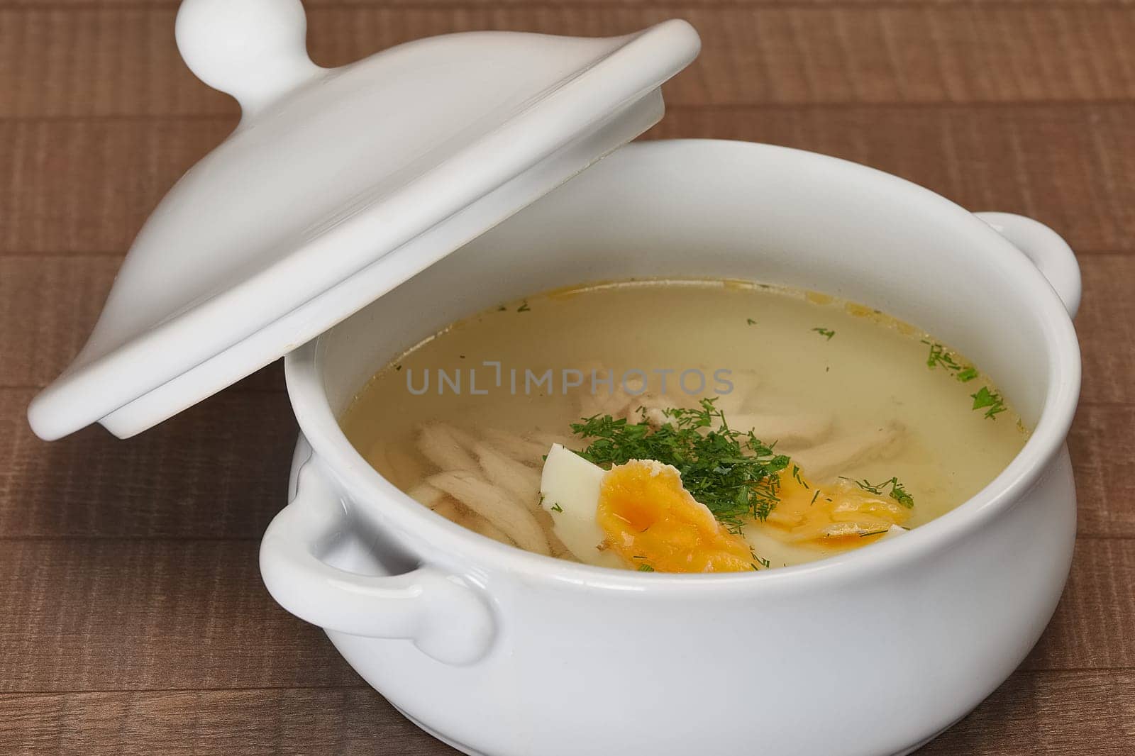 Chicken bouillon in the white bowl on the rustic wooden background. Clear  broth in a bowl.