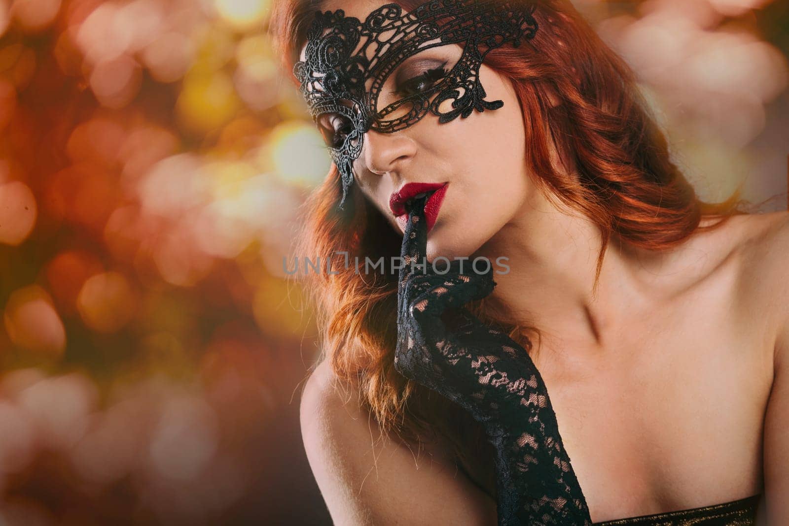 Closeup of sexy red haired woman with laced gloves and venetian mask in front of blur night lights. New year night and event party celebration. Luxury and glam lifestyle.