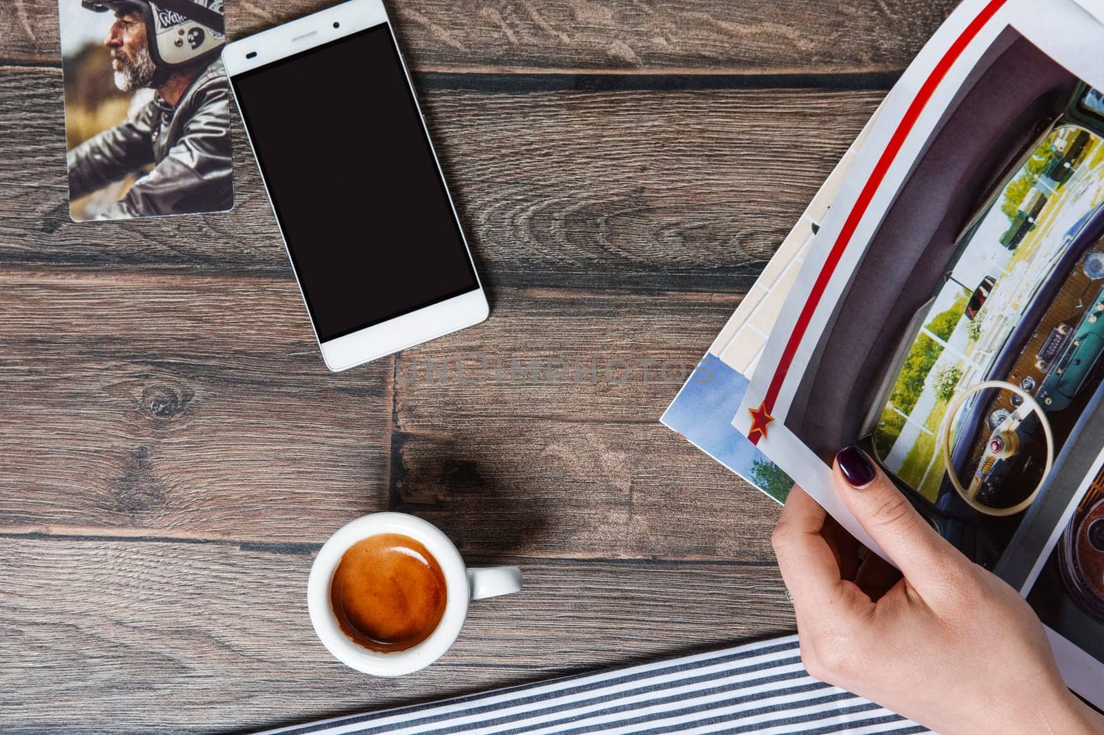 Top view of table with cup of coffee and smartphone. Hand holding magazine.