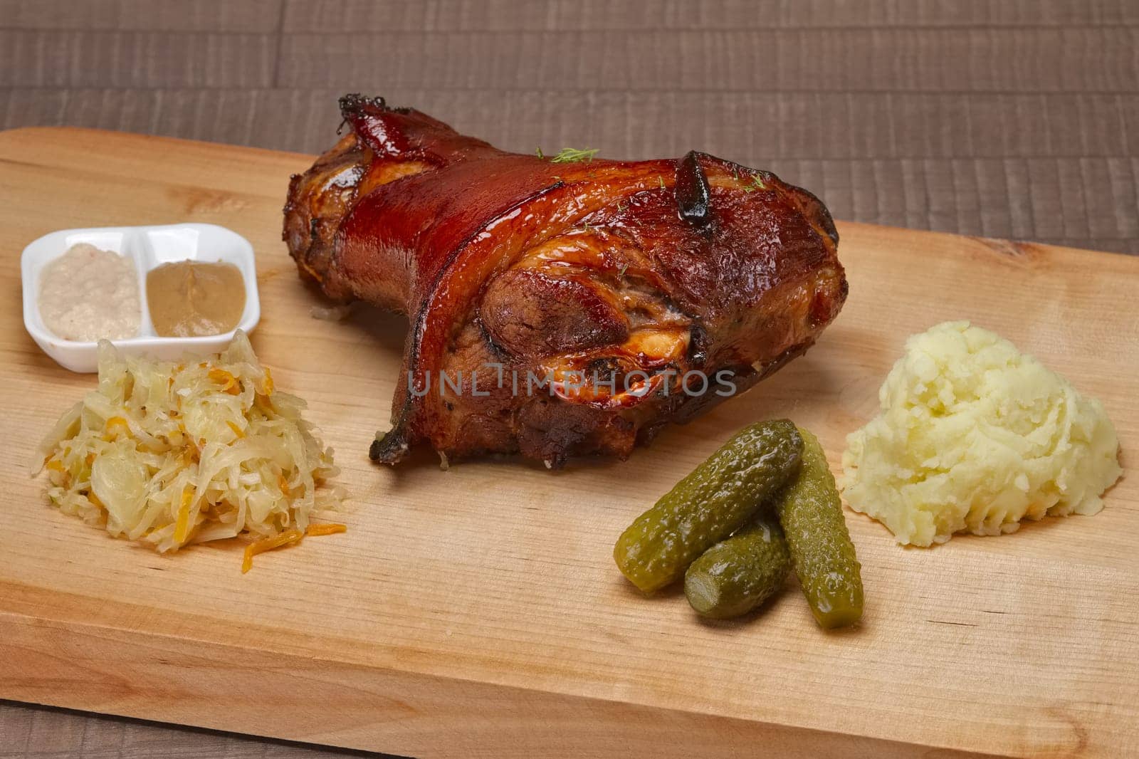 Roasted knuckle with mashed potato, sauerkraut, pickled cucumber and mustard with horseradish on wooden cutting board