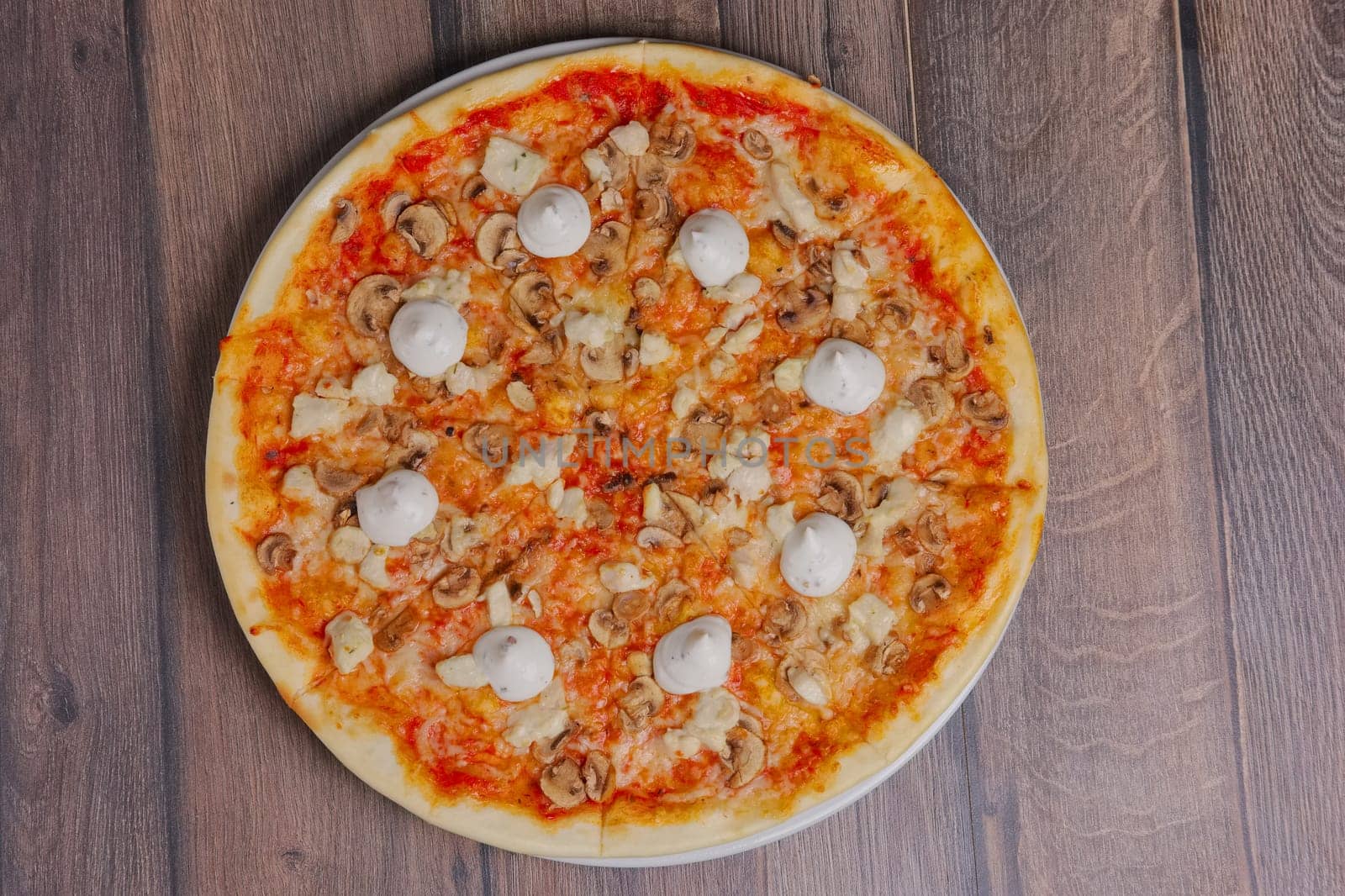 Top view of pizza with mushrooms and mayonnaise sause cutted on pieces.