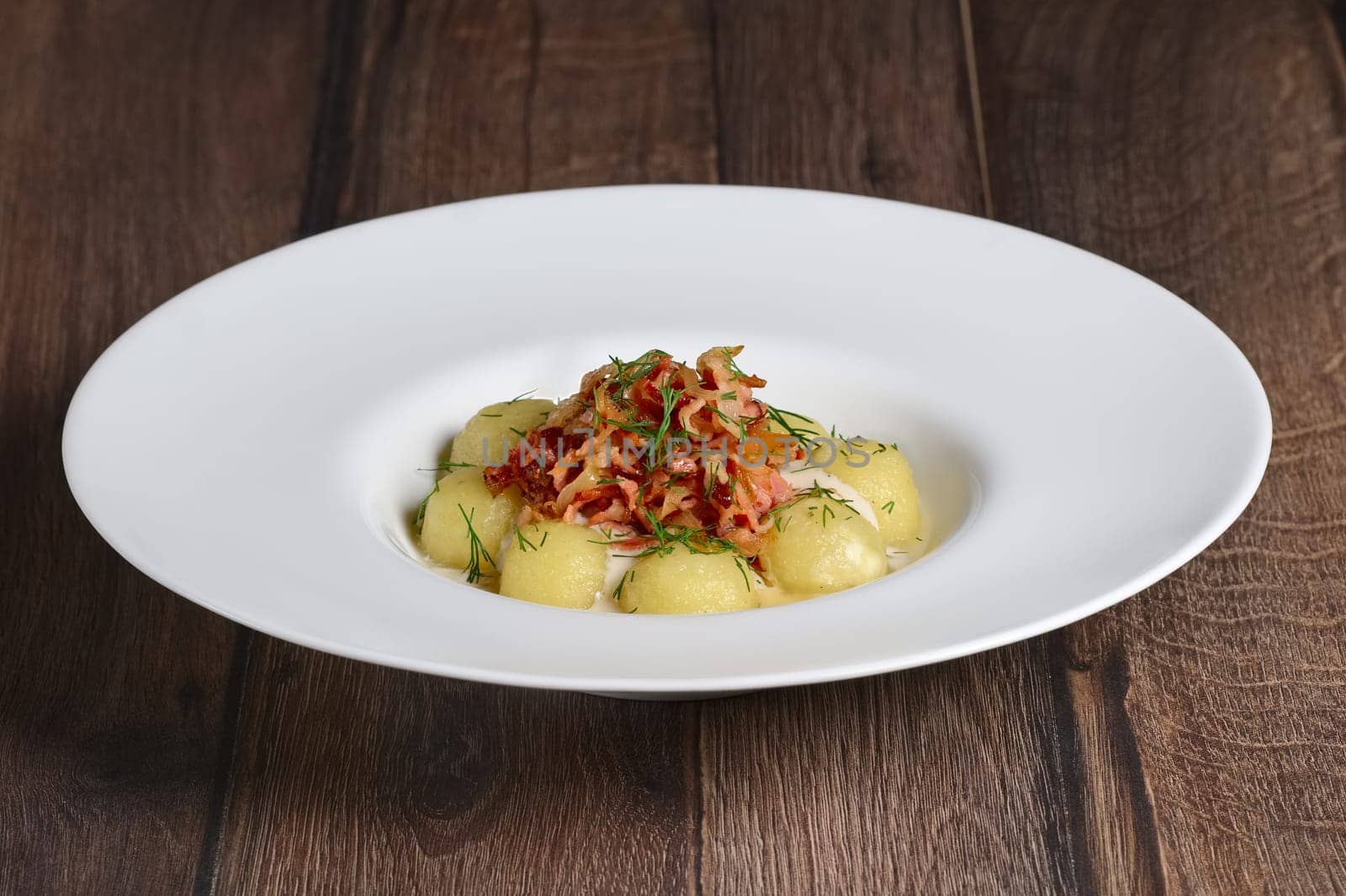 Plate with gnocchi, smoked bacon and cream sauce on wooden table.