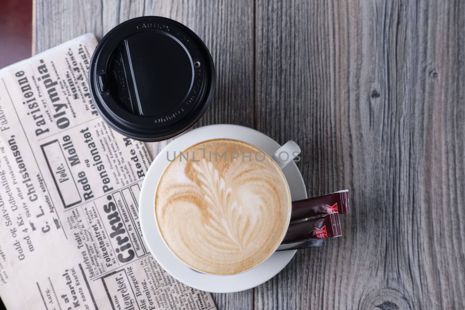 Ceramic and cardboard cup of coffee on wooden table near newspaper. Top view.