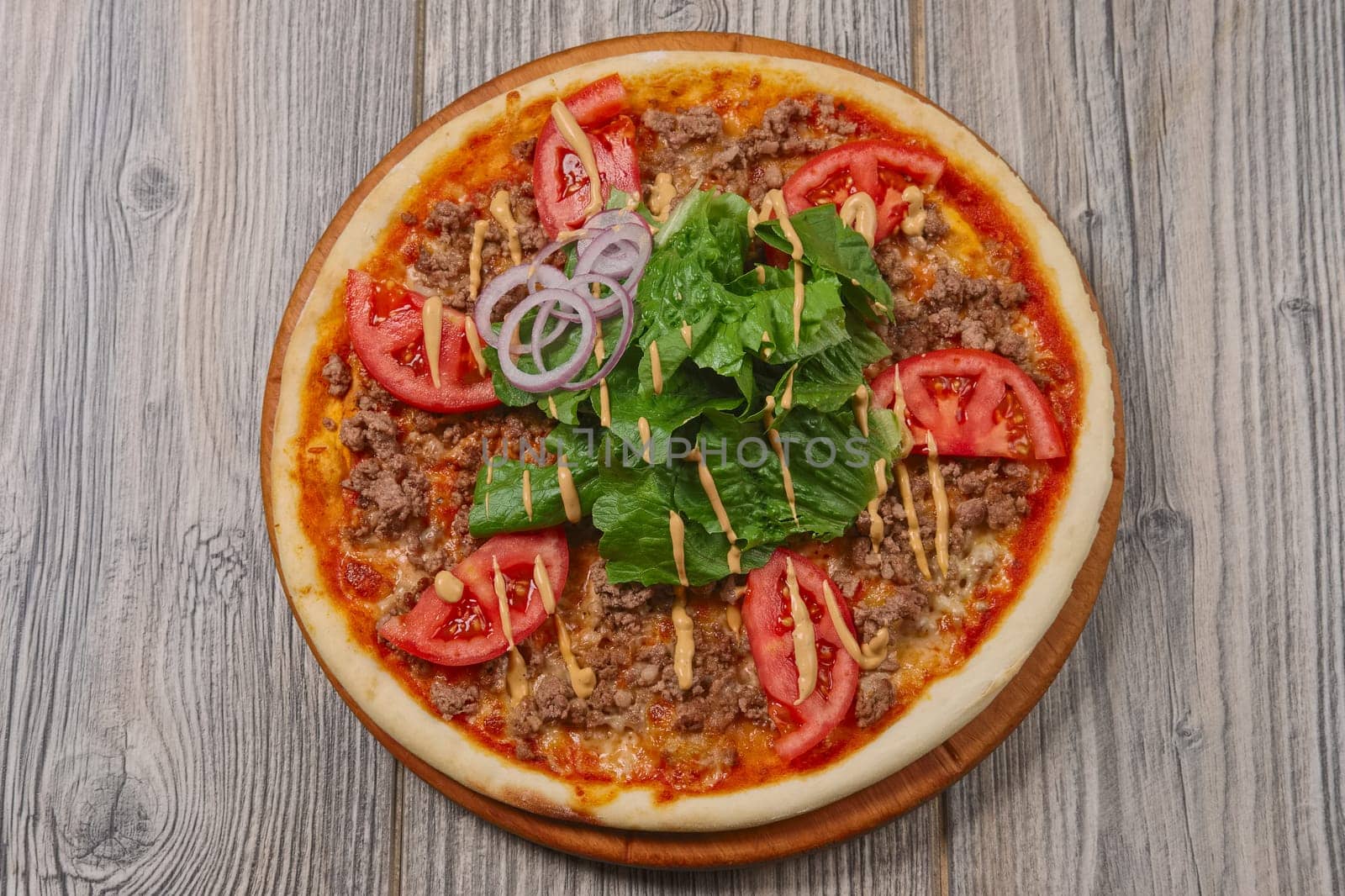 top view of pizza with meat, spinach, tomato and red onion on wooden table