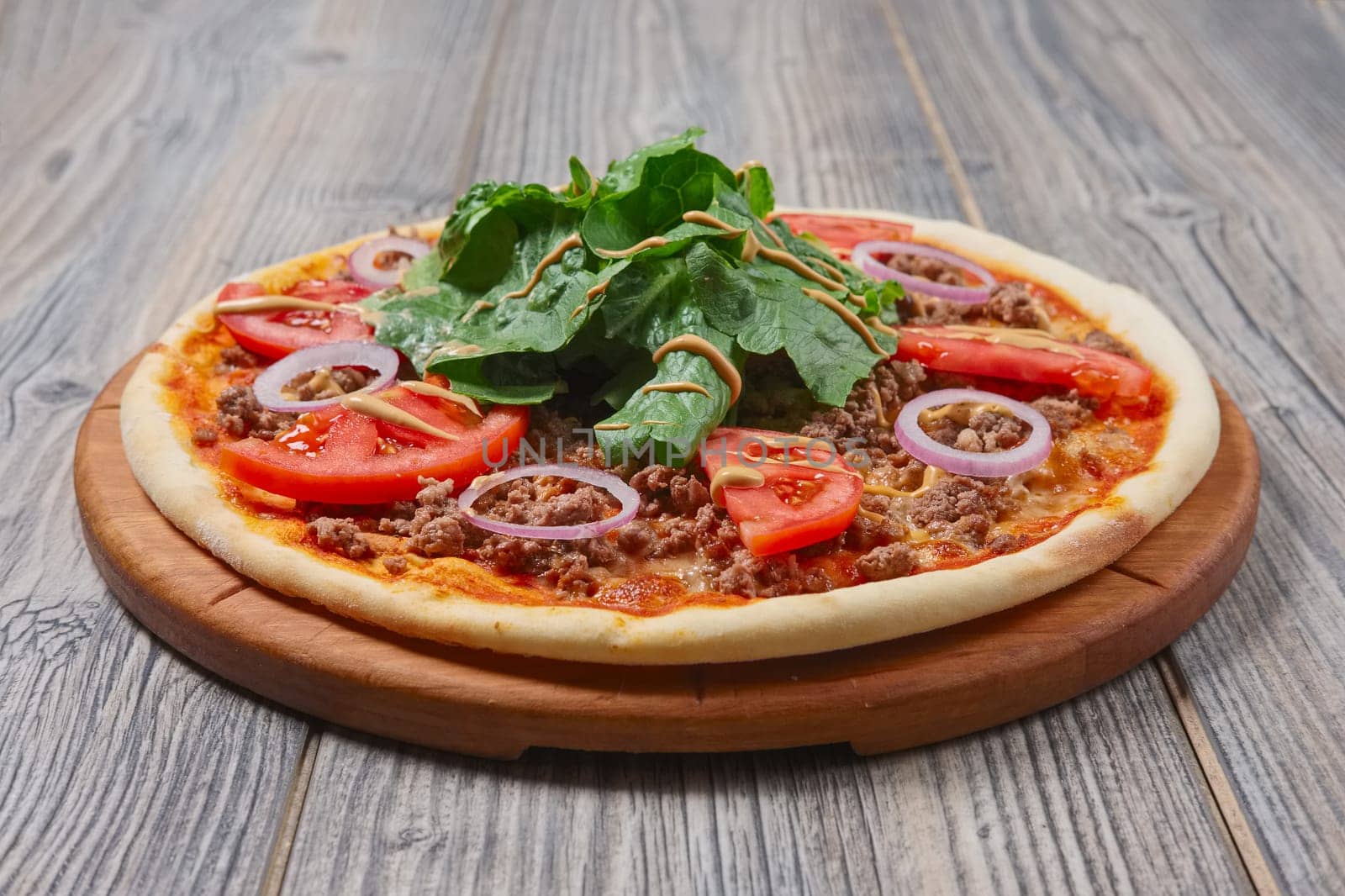 pizza with meat, spinach, tomato and red onion on wooden table