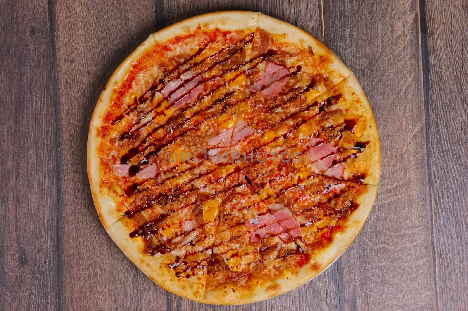 Top view of pizza with ham and balsamic sauce cutted on pieces.