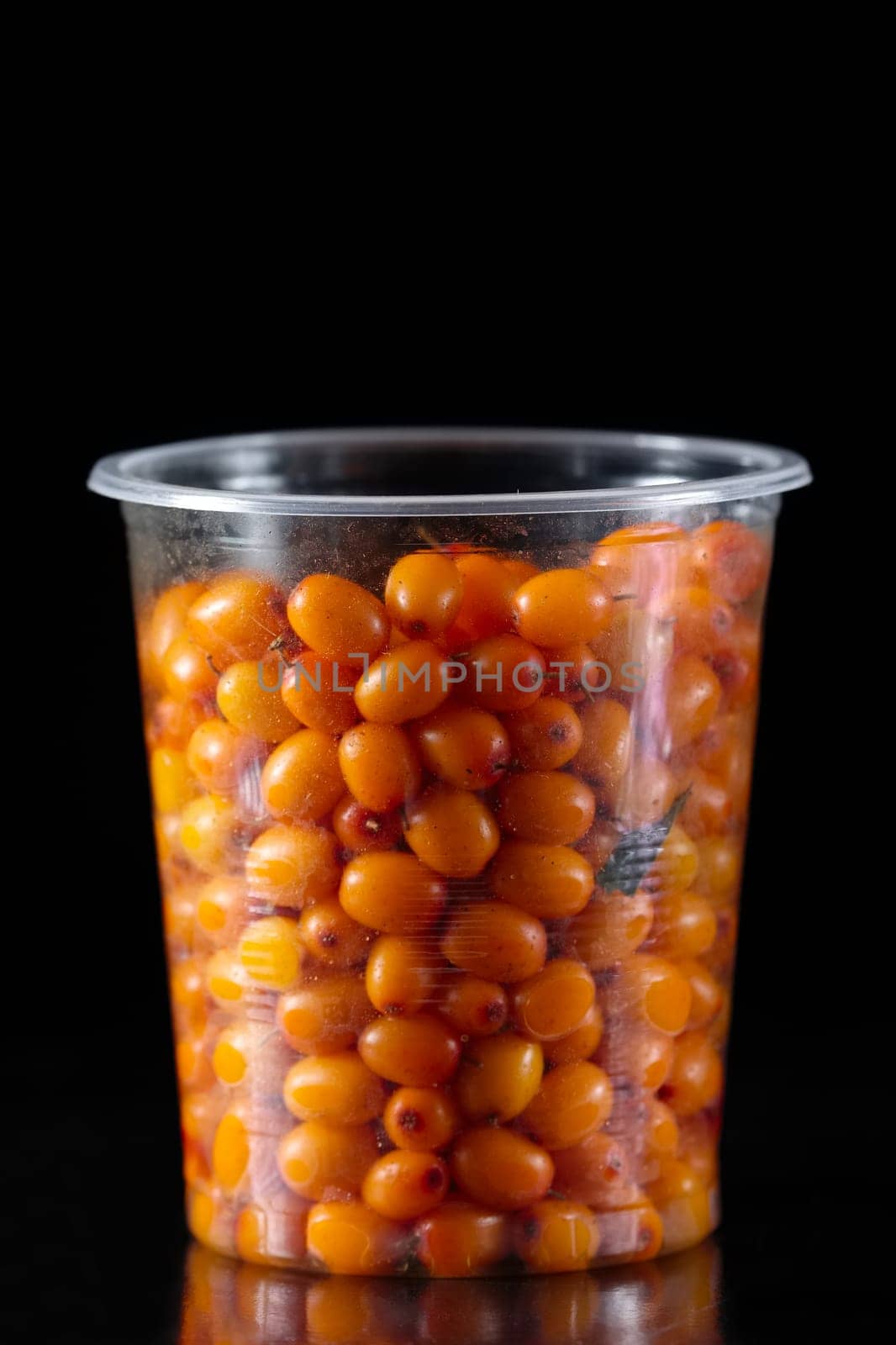 Plastic glass full of sea buckthorn on black background