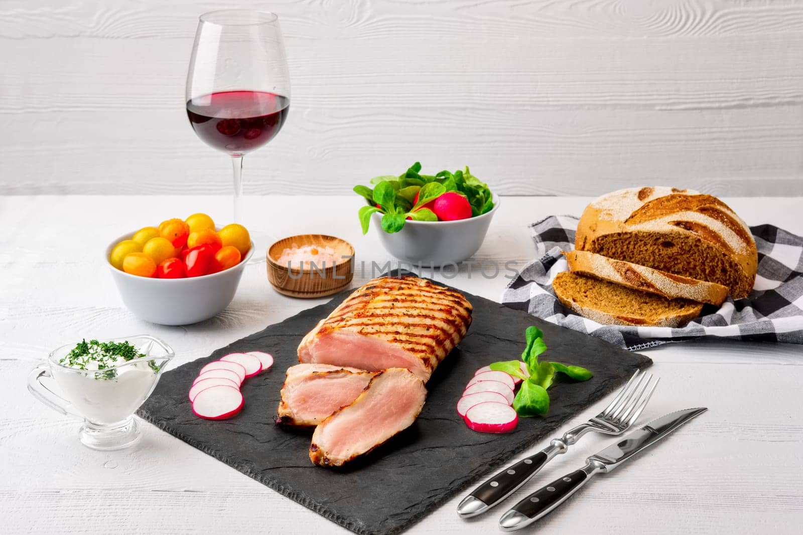 Sliced grilled pork fillet with fresh tomatoes and raddish served with glass of red wine.
