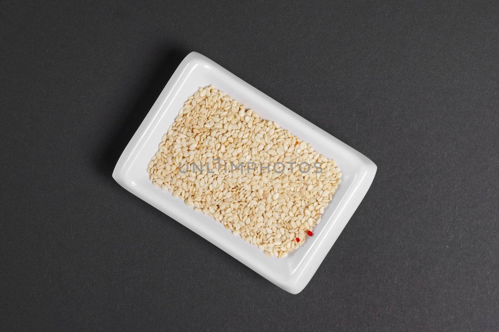 Top view of white sesame seeds in a little dish on gray paper