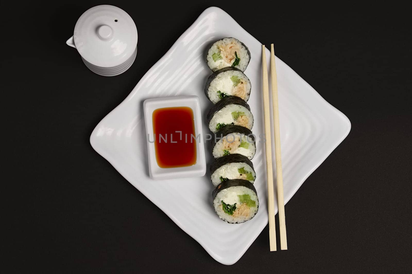 Top view of portion of chicken teriyaki rolls served on black paper with soy sauce and hashi.