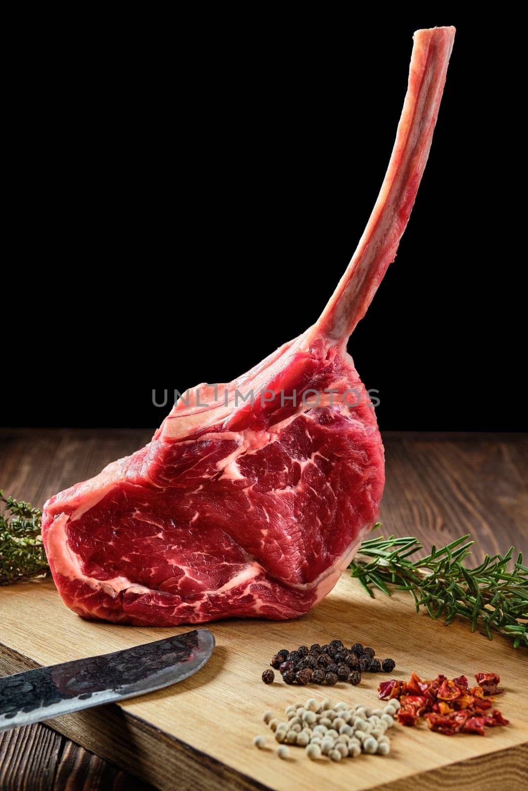 Close up of raw cowboy steak on wooden cutting board with spice