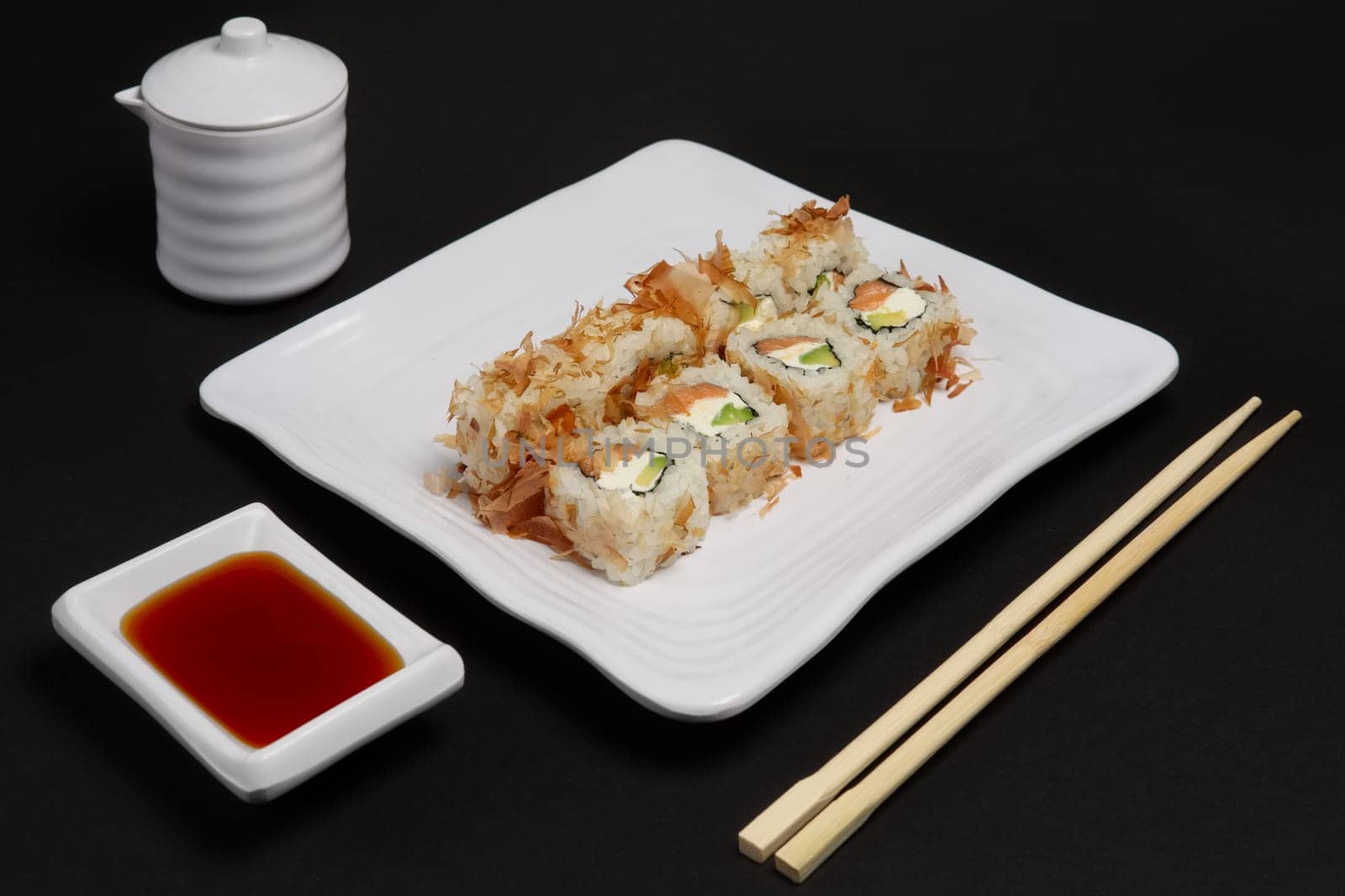 Portion of bonito rolls served on plate with soy sauce and wooden hashi.