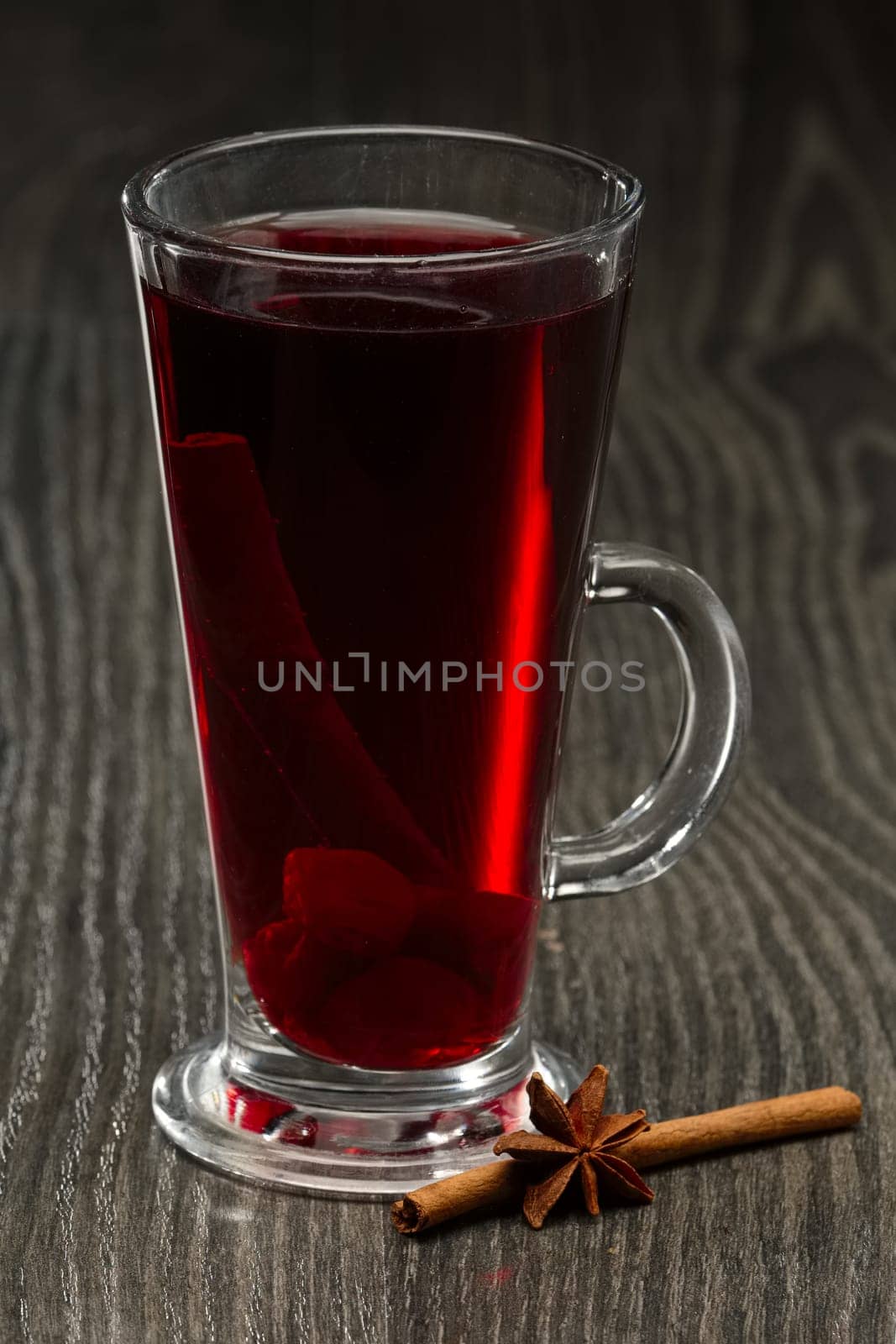 Glass of hot cherry tea with cinnamon on wooden table on dark wooden table