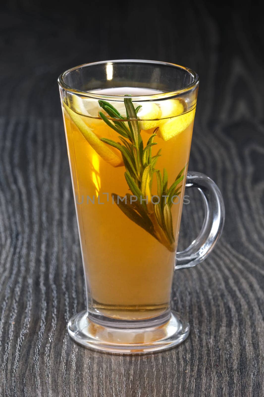 Transparent glass of rosemary, lemon and honey tea on wooden table