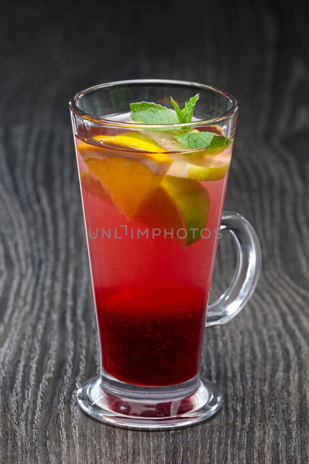 Tall transparent glass with raspberry and citrus tea on dark wooden table