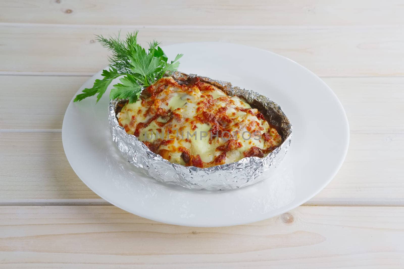 Meat baked in foil with vegetables and cheese on wooden table