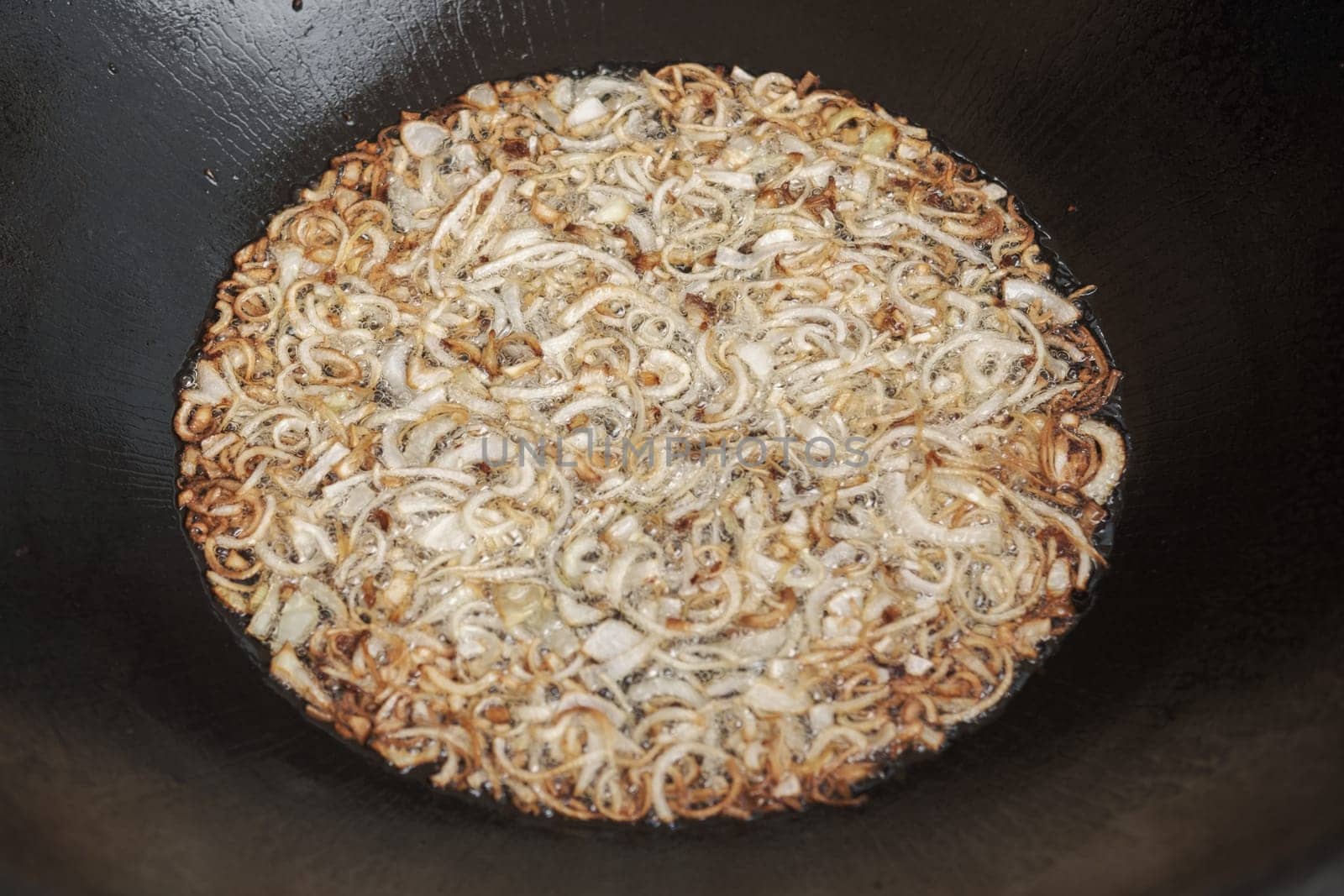 Frying onion in oil in cauldron. The making of pilaf, step by step.