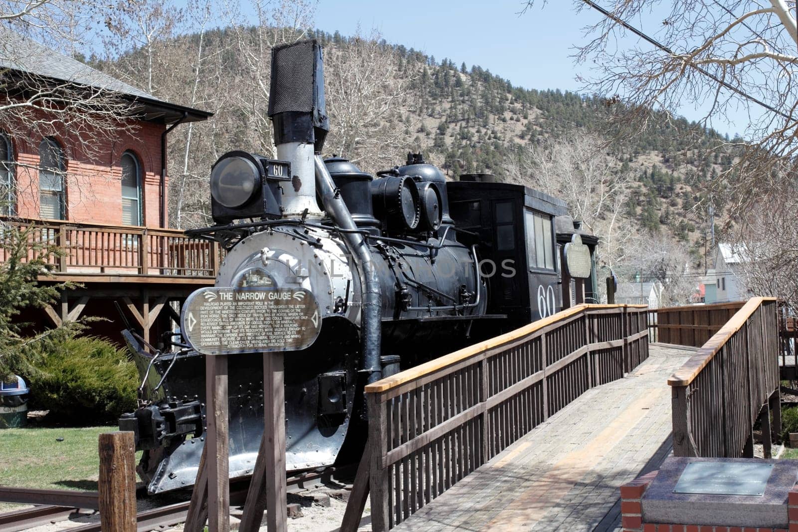 Idaho Springs, CO, USA - April 23, 2014: Front and side view of an old black train with historical information on a wood sign. A wooden walkway travels the length of the historical train to get a better closeup view.