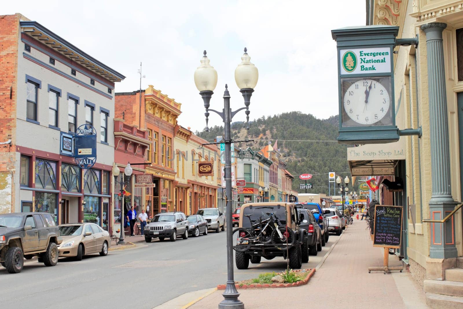 Idaho Springs, CO, USA - April 21, 2014: People shop in  historical buildings stores, restaurants and more enjoying the spring day on Miner Street in downtown. Many old and colorful buildings line both sides of the main street with many people and vehicles.