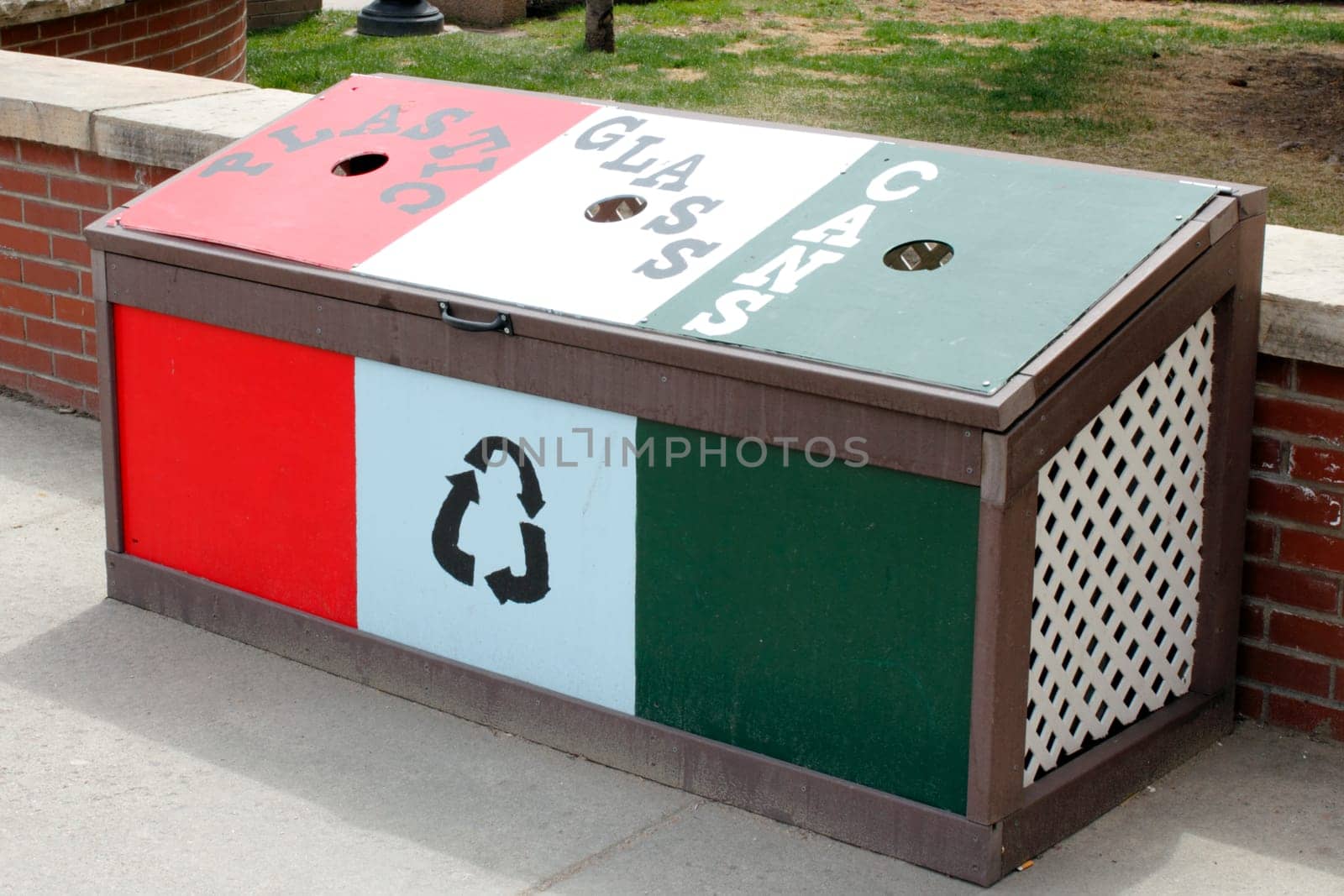 Idaho Springs, CO, USA - April 21, 2014: Hand painted wood bin in red, white and green to recycle plastic, glass and cans located on a sidewalk in front of Citizens Park on Miner Street.  A recycle bin center for plastic, glass and cans on a sidewalk in front of a a low brick wall during the day.