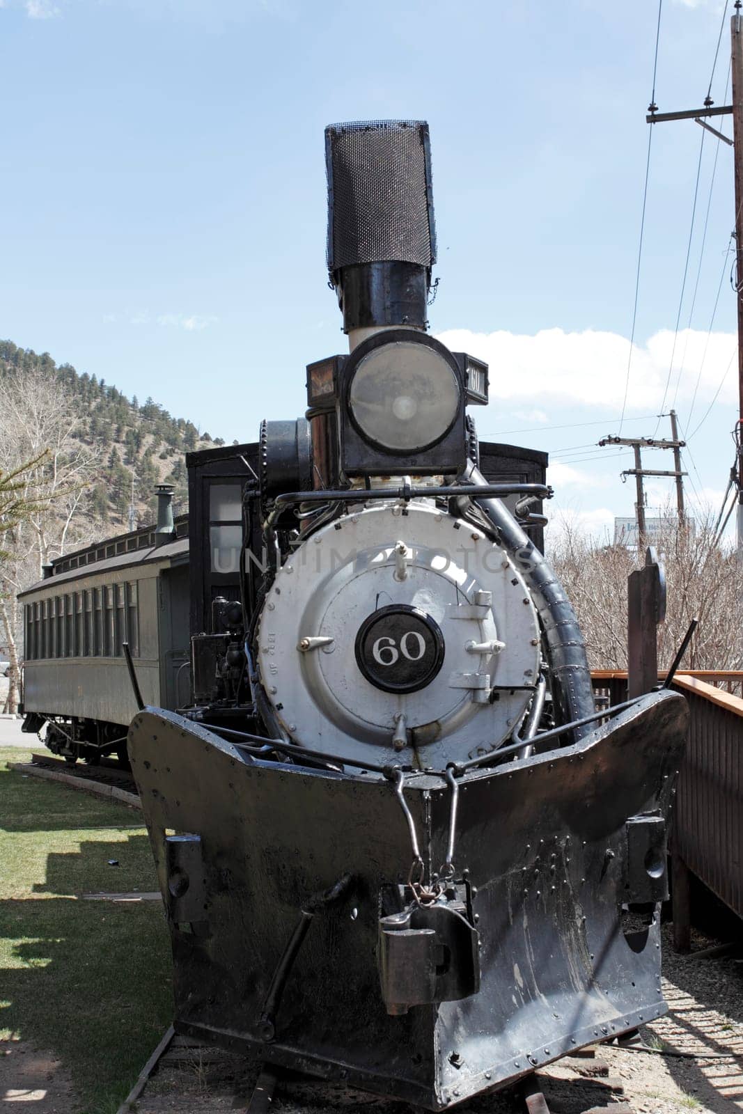 Idaho Springs, CO, USA - April 23, 2014: A black antique railroad train on a track at a public museum outdoors on a sunny day. The front of a vintage train engine and caboose behind it on a railroad track outside.