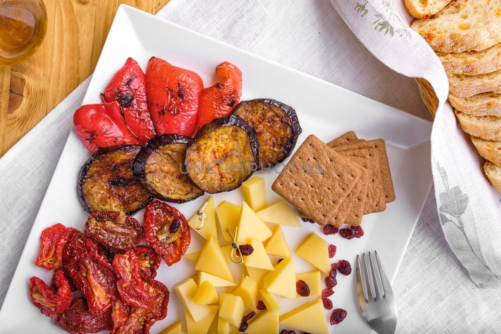 Overhead view of set of various appetizers for wine - cheese, sun-dried tomatoes, roasted eggplant, bell pepper, hardtack and dried cranberry