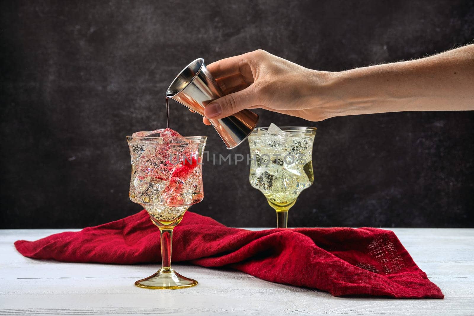 Hand of bartender with jigger pouring pomegranate bitter in cocktail with gin