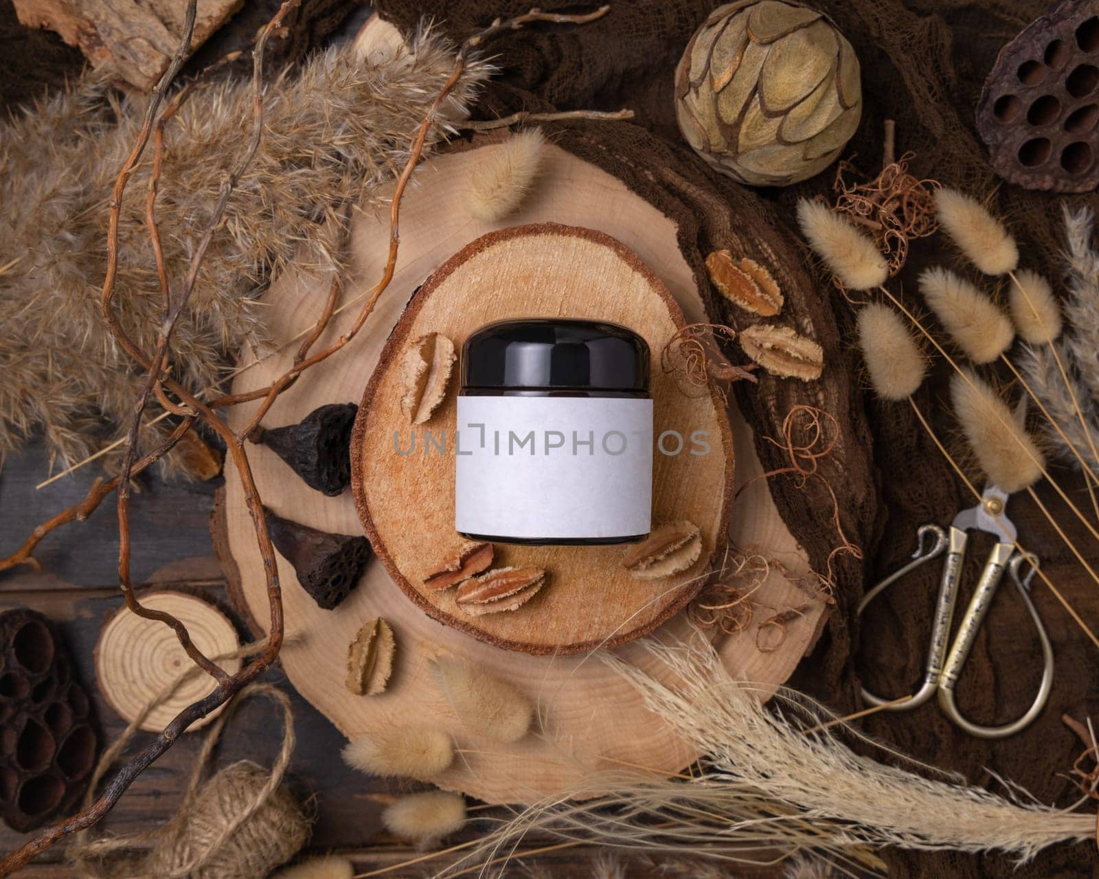 Cream jar with blank label on wood near natural boho decorations top view, cosmetic packaging mockup. Skincare product for everyday beauty routine. Bohemian eco friendly flat lay with dried leaves.