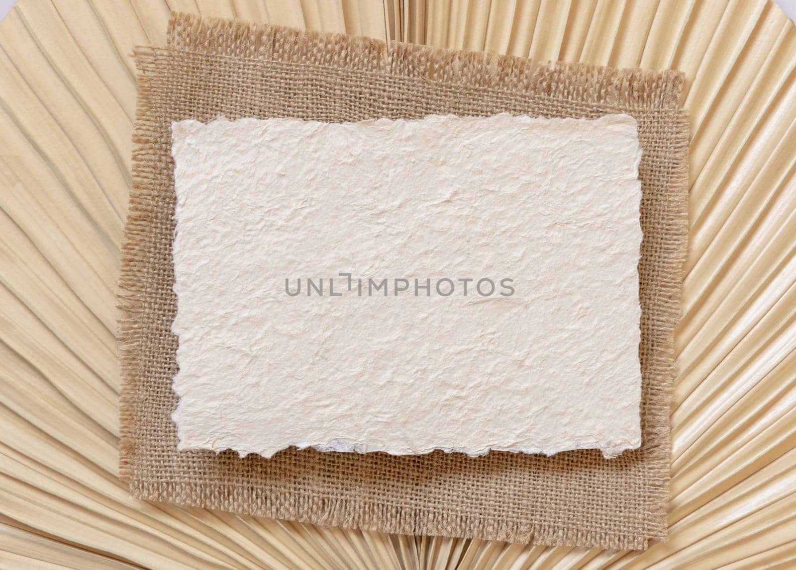 Blank handmade paper card on dry beige palm leaf near hare's tail grass top view, mockup. Boho scene with horizontal card. Bohemian or close to nature greeting card or wedding Invitation.