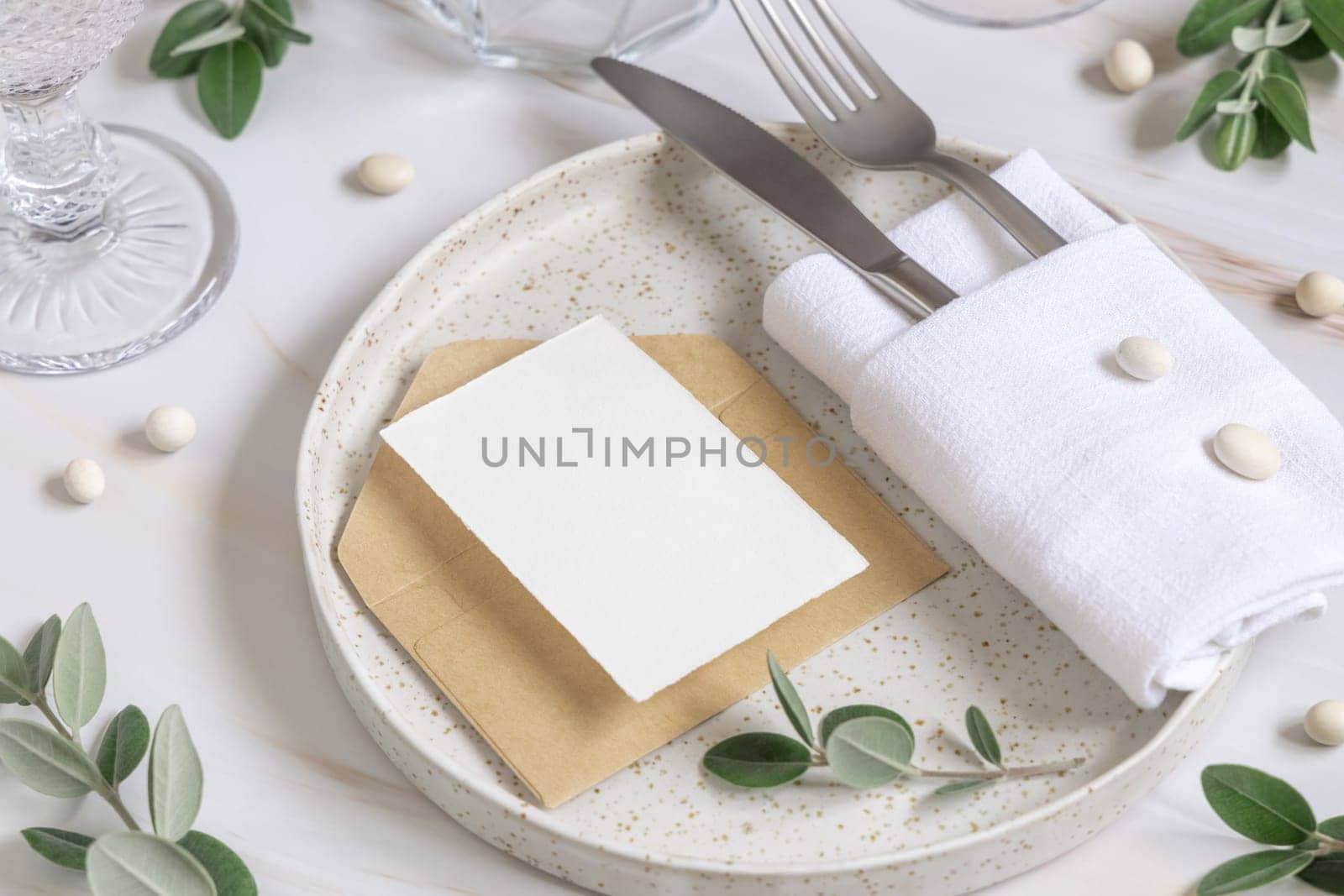 Elegant Table setting with card and envelope decorated with eucalyptus branches close up, Wedding Mockup. Romantic table with vertical paper card. Close to nature and simplicity concepts