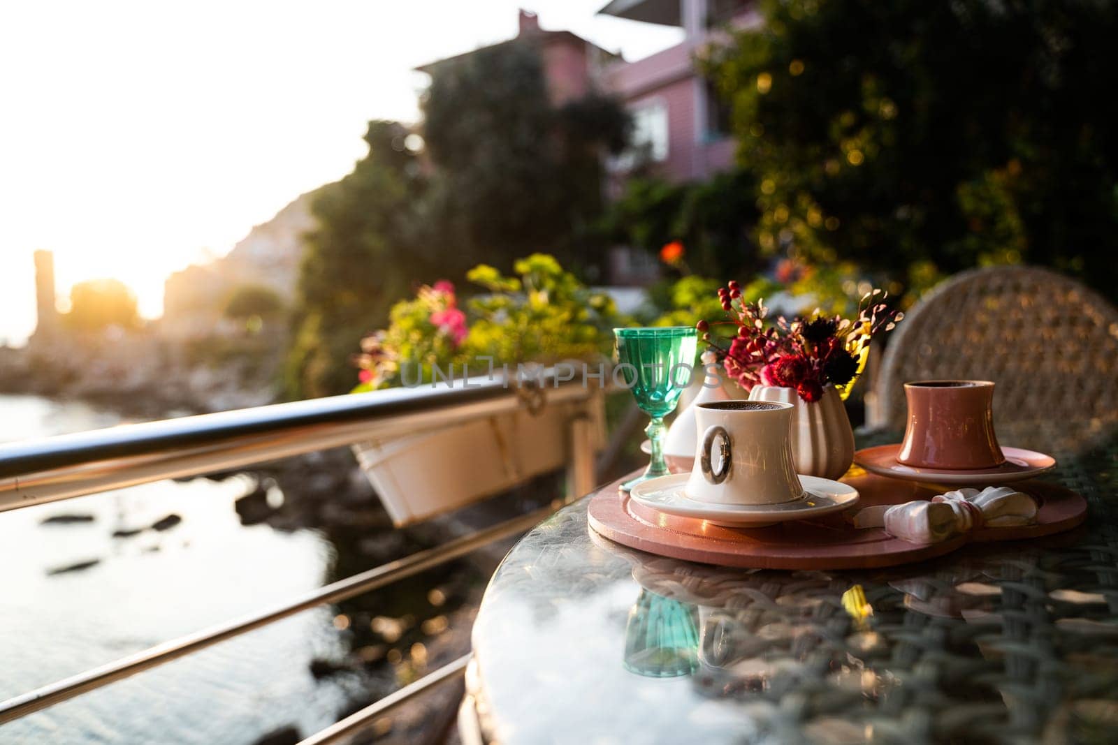 front view closeup of traditional Turkish coffee cups served outside with water flowers and delight dessert in romantic setup on glass table at sunset