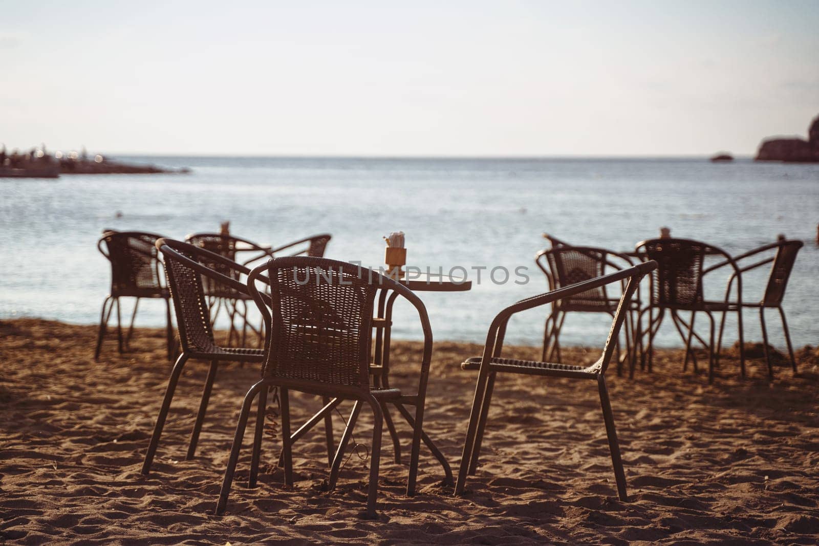 rear view closeup of empty cafe table and chairs on sandy beach in front of romantic sea golf with clear sky before sunset